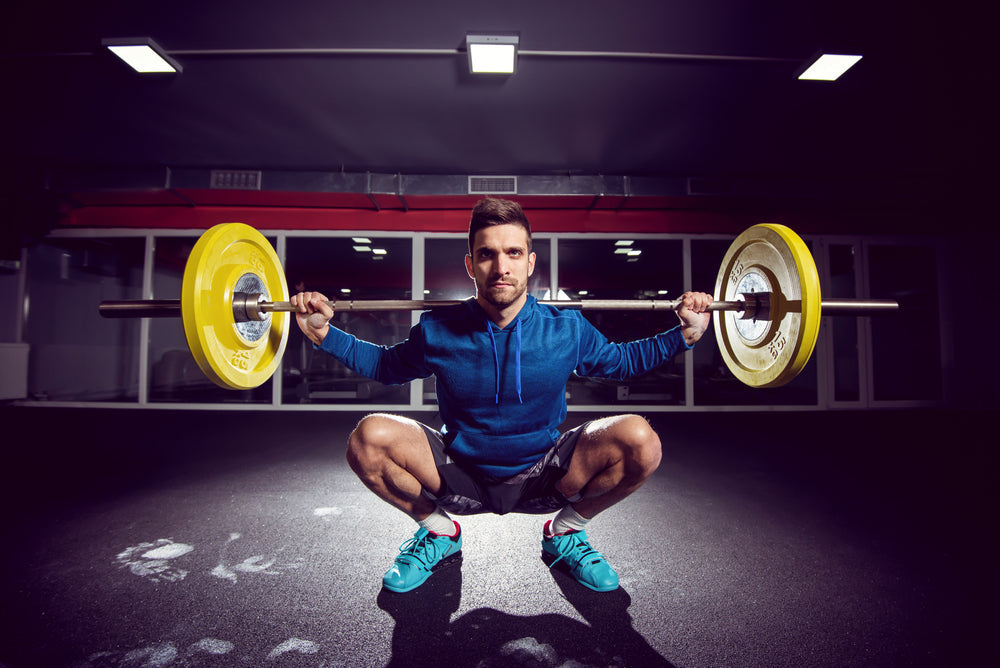 man doing barbell back squats in a gym
