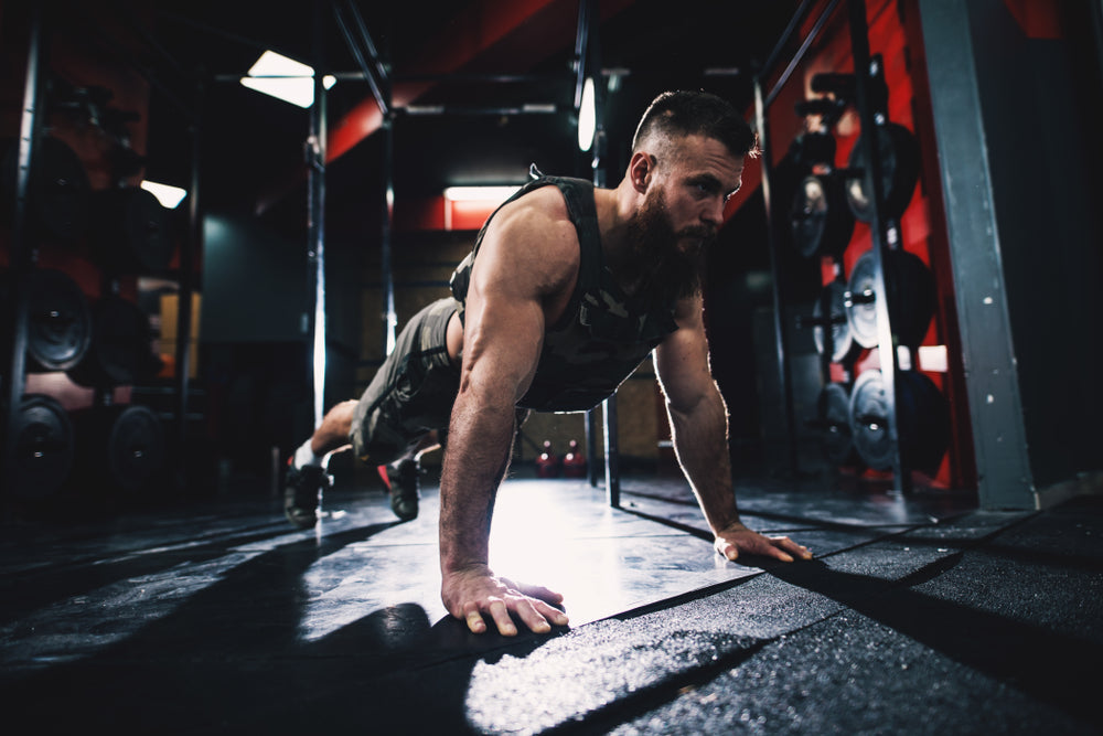  bodybuilder guy in military vest doing push-ups exercise in the gym.
