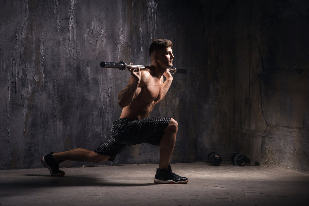 fit muscular man doing barbell walking lunges in a studio