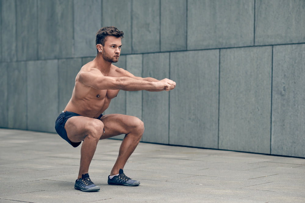 Fit muscular shirtless young man doing bodyweight squats outdoors