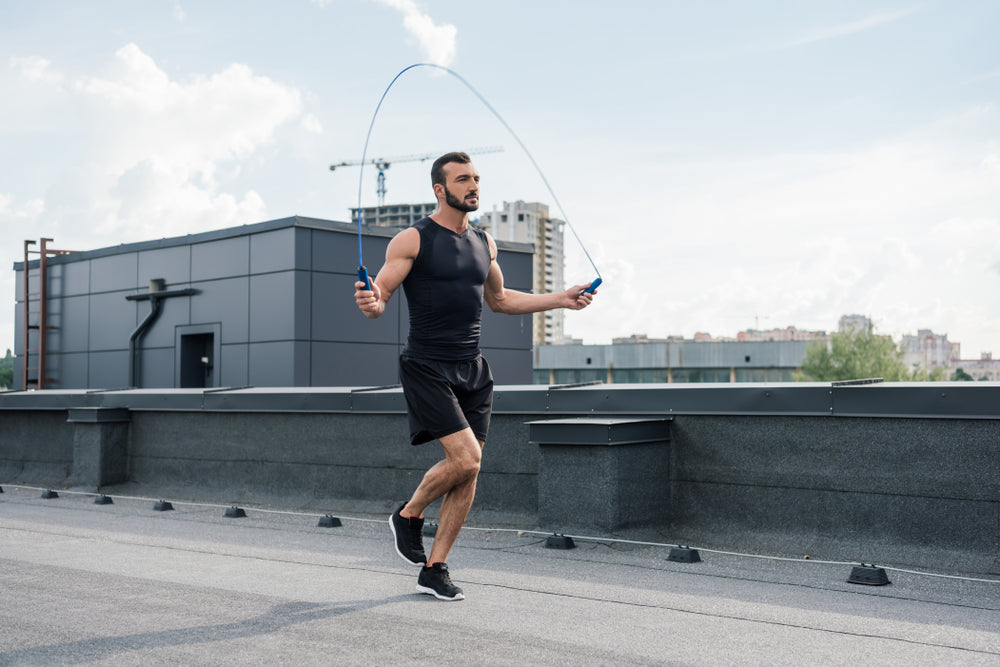 handsome sportsman training with jumping rope on roof