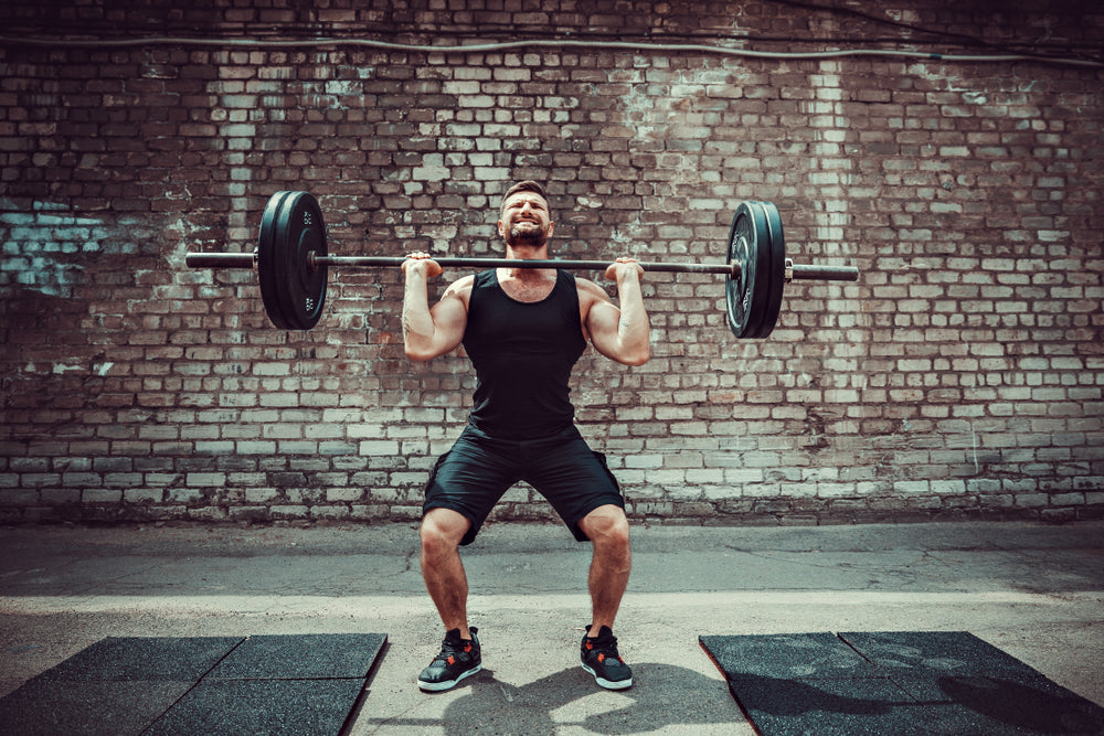 Muscular fitness man doing deadlift a barbell over his head in outdoor, street gym