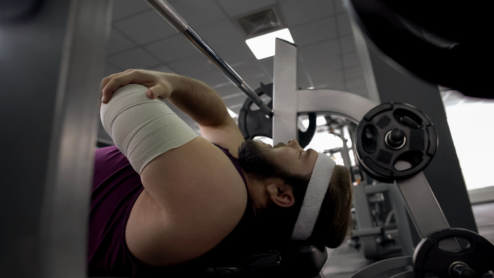 Injured man in gym feels sharp pain in arm after lifting barbell on bench press