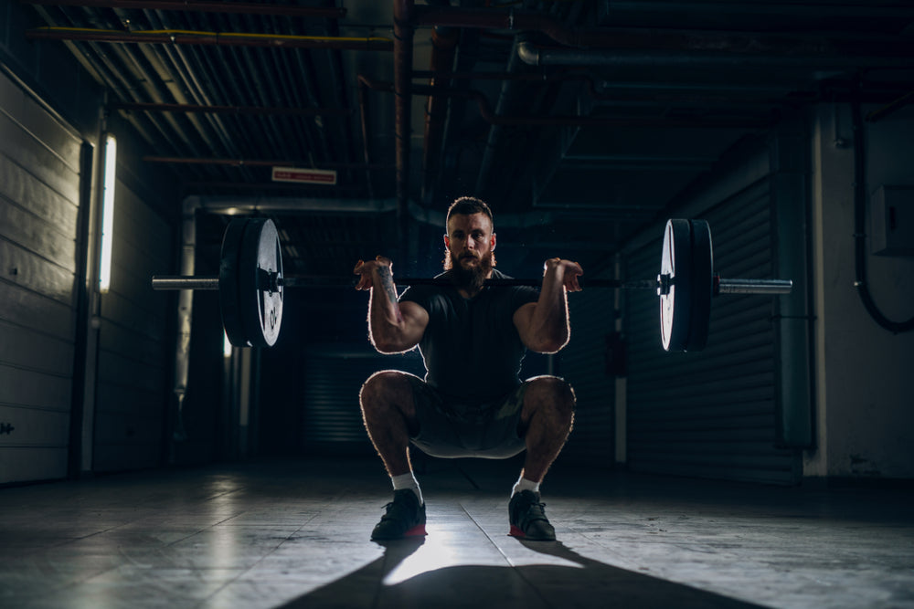 Muscular attractive caucasian bearded man doing front barbell squat in underground hallway