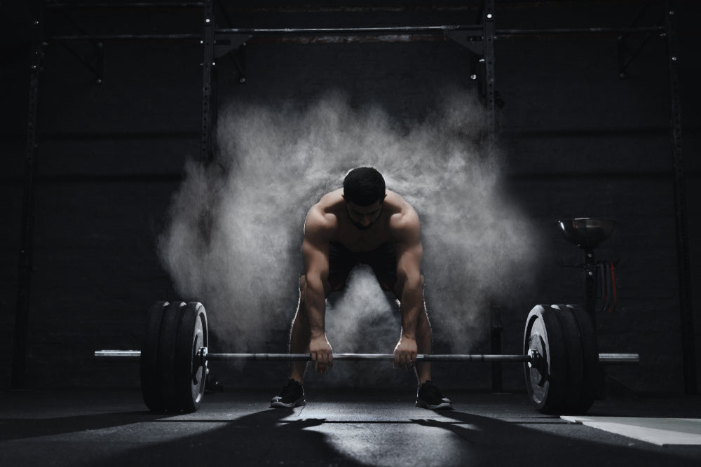Crossfit athlete preparing to lift heavy barbell in a cloud of dust at the gym.