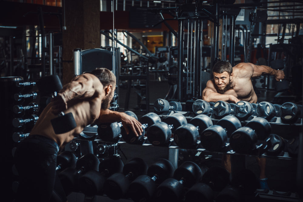bodybuilder doing triceps kickback lifting dumbbells in front of the mirror