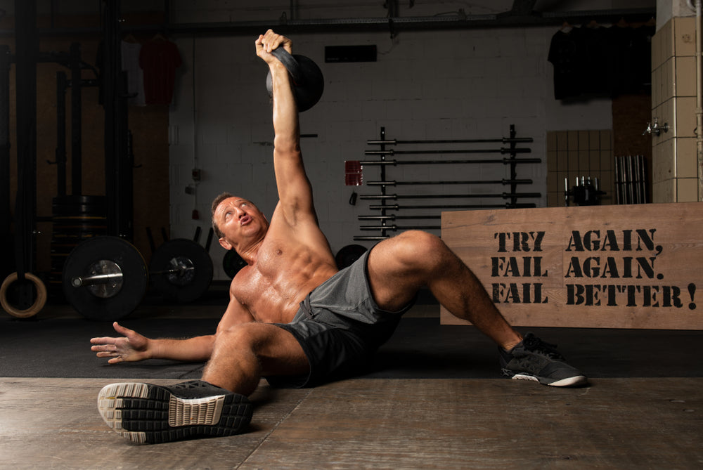 athlete with strong abs doing turkish get up with kettlebell in gym