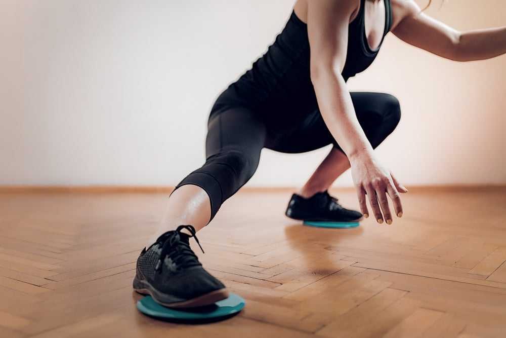 fit woman doing a Gliding Disc Exercise on wooden floor