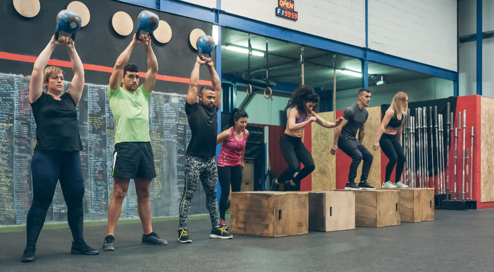 Group of athletes doing emom training with kettlebells and box jumps 
