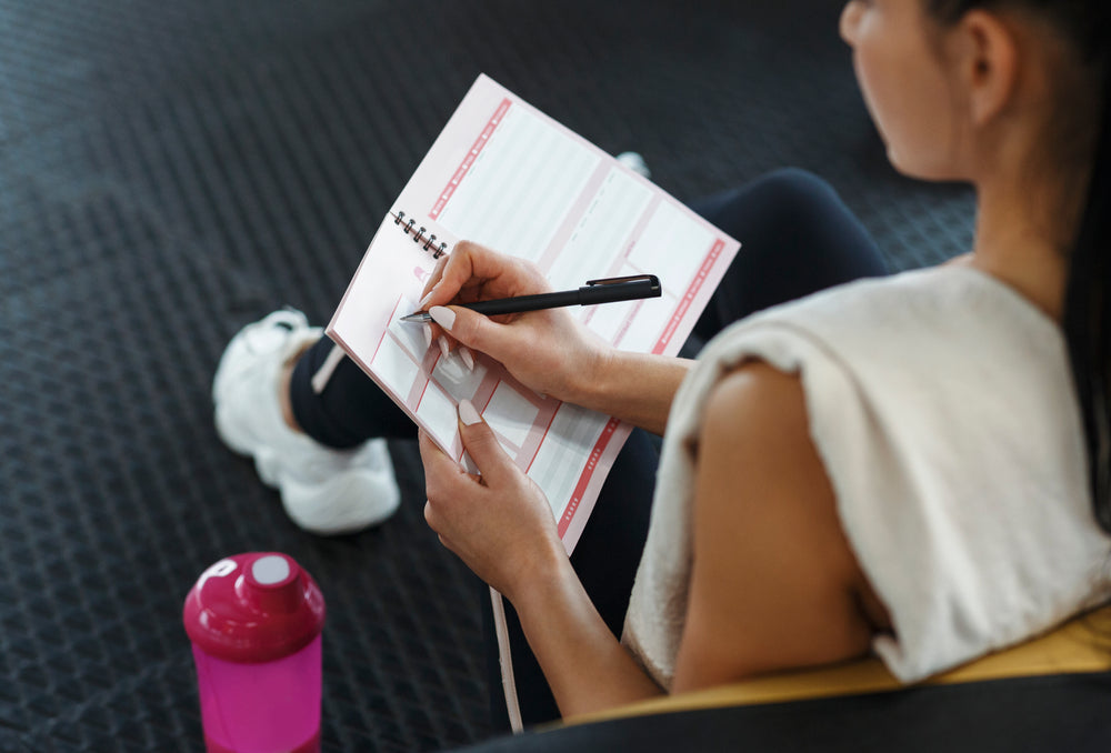  Young woman making her workout schedule in notebook indoor