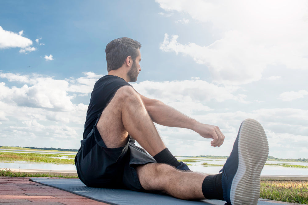 Man wearing a black shirt and dark green shorts laying forward in hip stretching pose