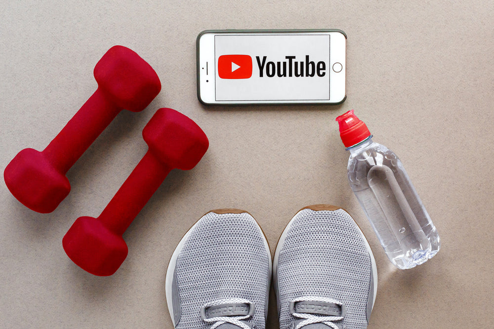 a smartphone with the YouTube logo, gray sneakers, red dumbbells and a bottle of water