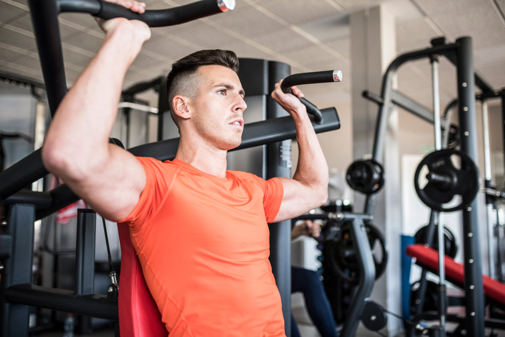 Young fit man doing shoulder press machine exercise at gym