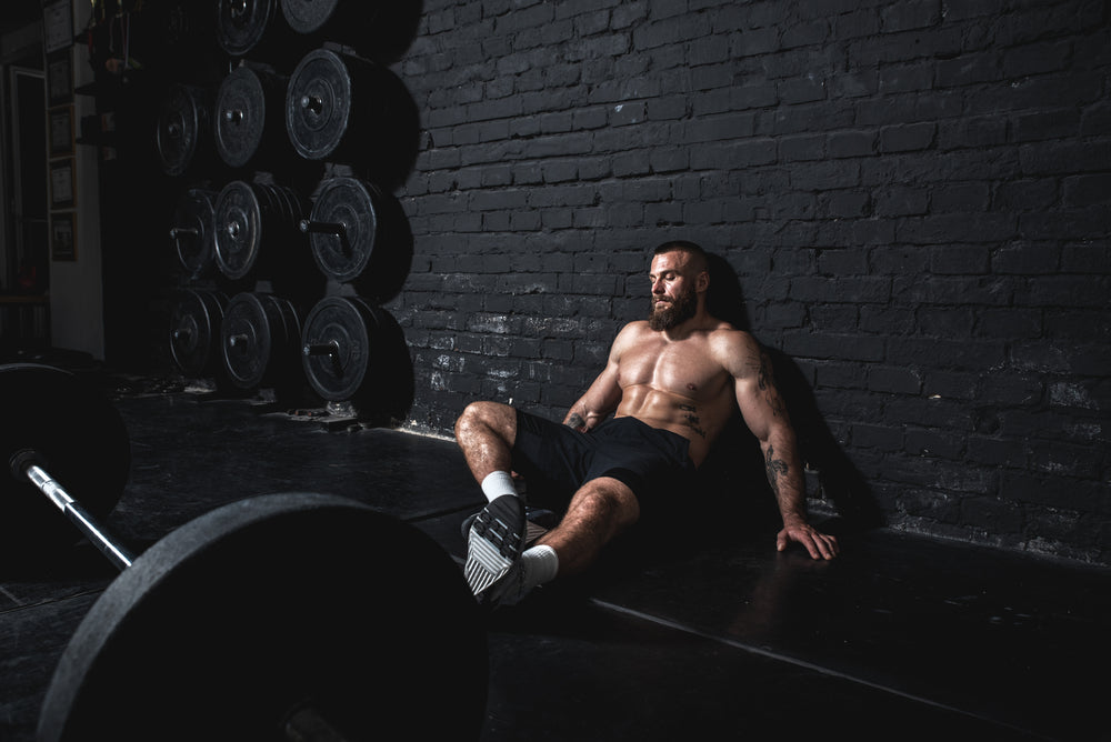 Young active strong fit sweaty muscular man wit big muscles sitting on the floor of the gym after barbell weight lifting workout