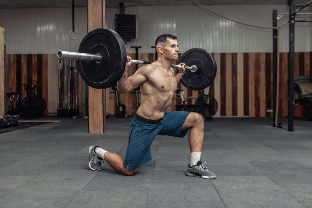 Young muscular male bodybuilder doing lunges with a barbell on his shoulders