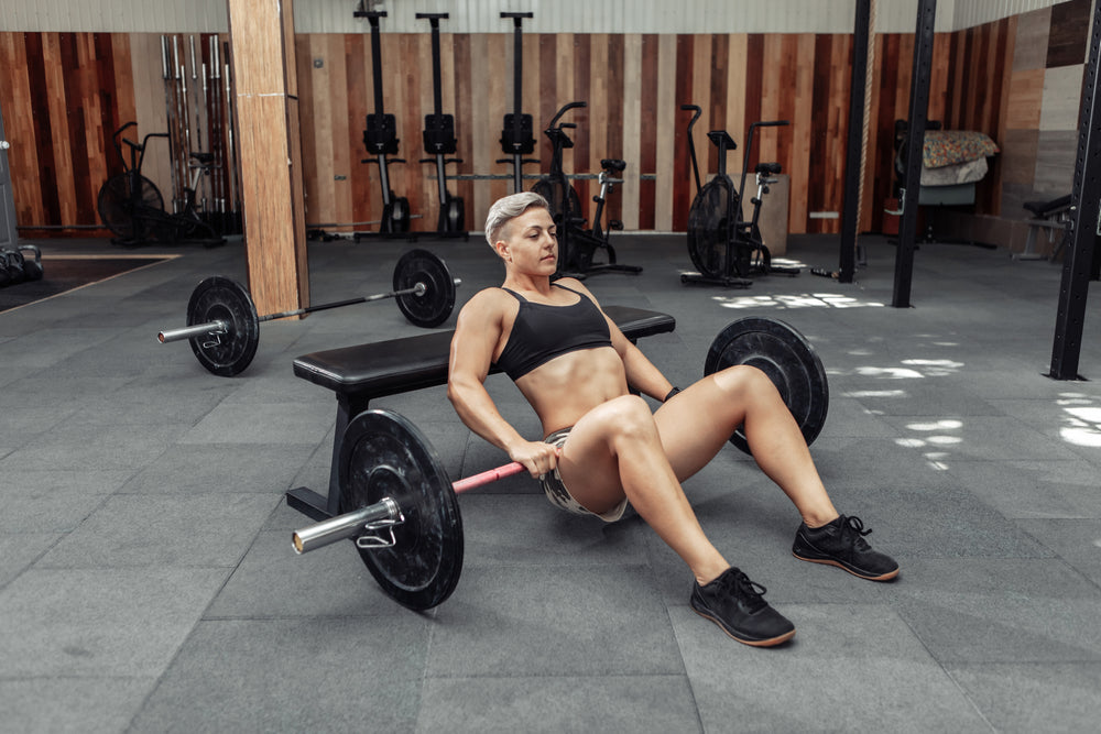 Young athletic strong woman practicing glute bridge exercise with a heavy barbell