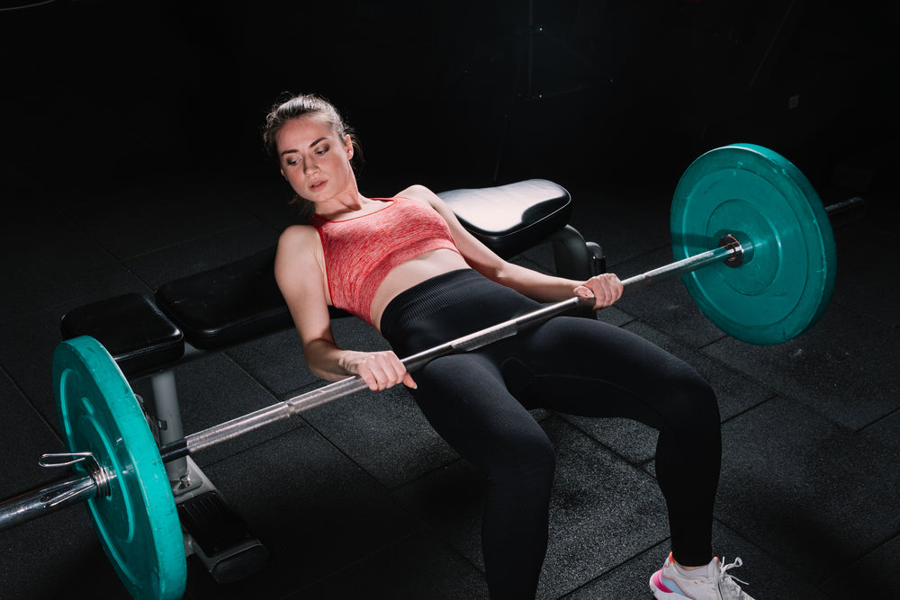 Young beautiful woman doing a barbell hip thrust on a bench