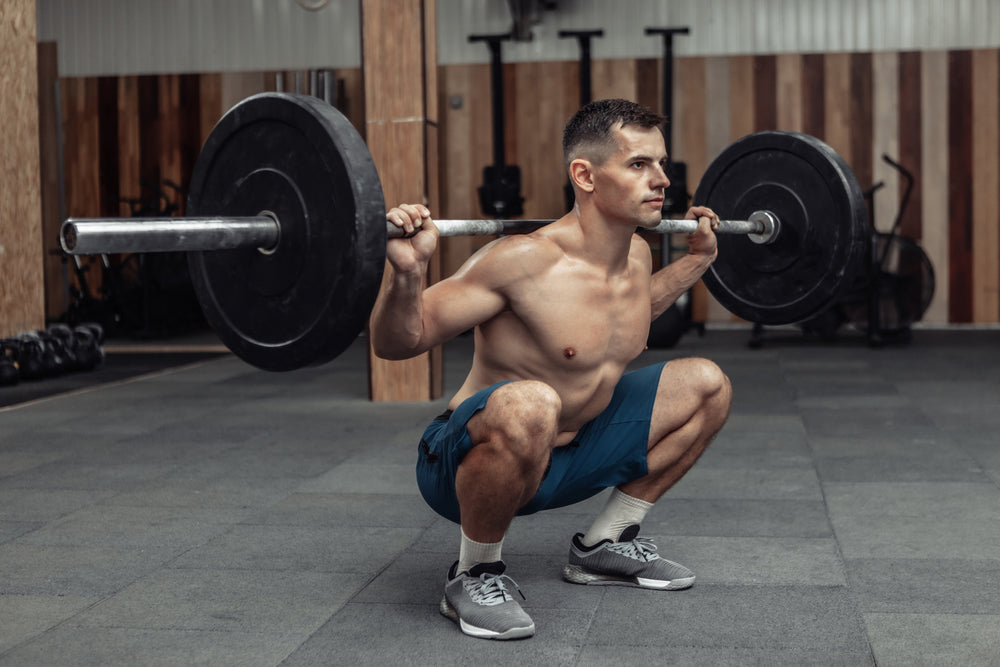 Young muscular male bodybuilder doing squats with a barbell on his shoulders in a modern health club