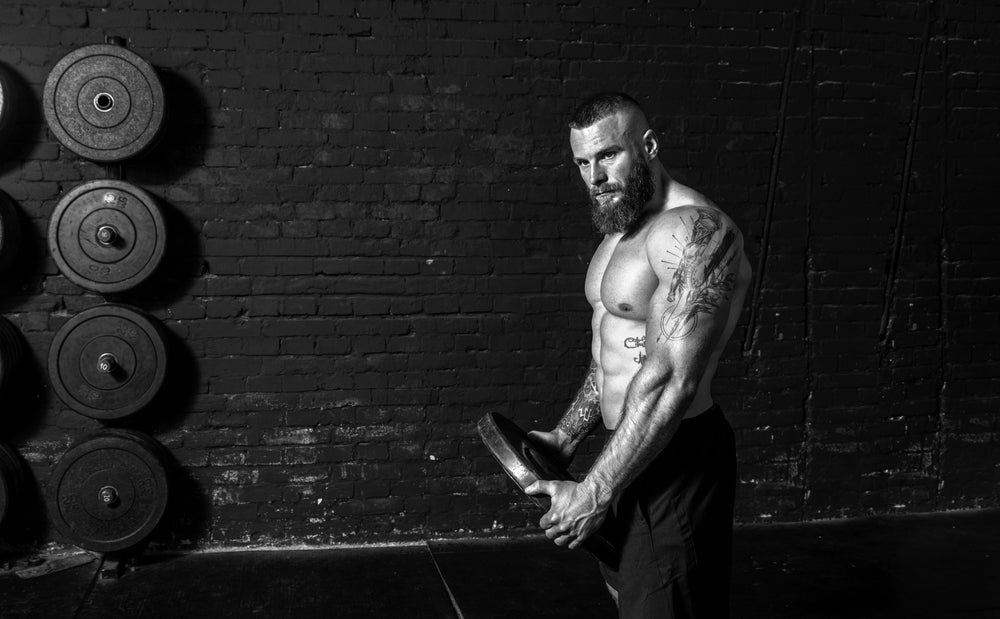 Young active sweaty strong muscular fit man with big muscles holding heavy barbell weight plate in his hands