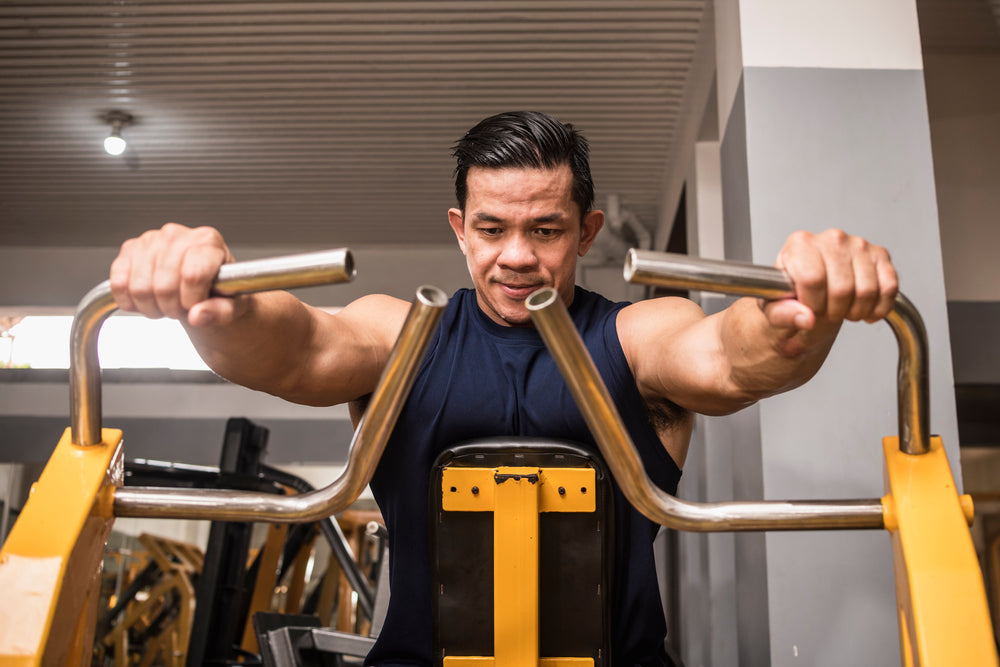  man in a blue tank top does seated machine rows at the gym