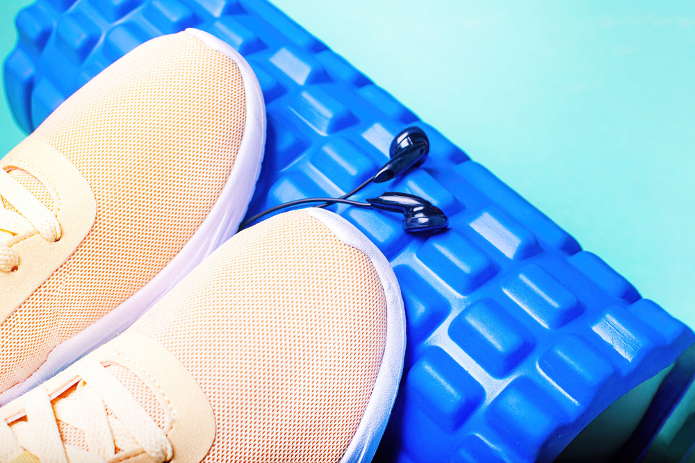Peach sneakers, headphones and a massage roller on green background.