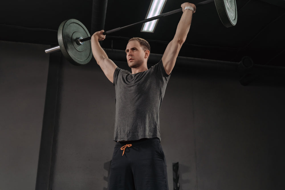 Strong muscular man holding heavy barbell overhead press at the gym