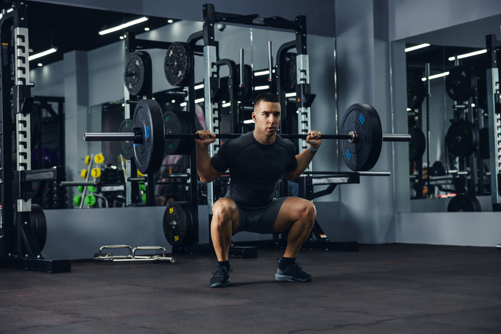 A side portrait of a bodybuilder in grey doing squats using a barbell in a gym to train his legs and back.