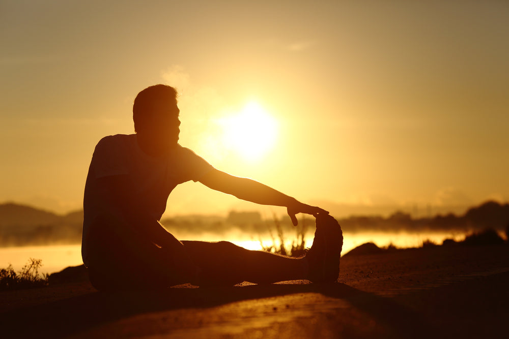 Silhouette of a fitness runner man stretching at sunset with the sun in the background