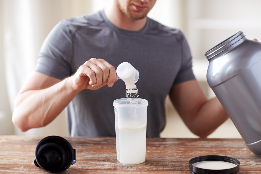 close up of man with jar and bottle preparing protein shake