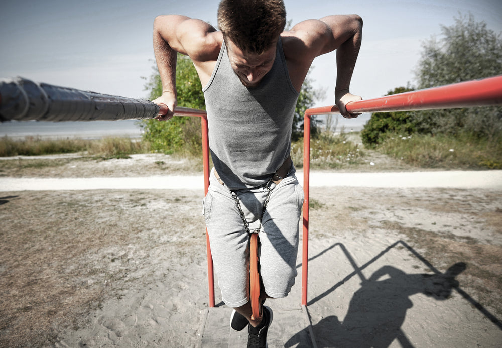  young man doing triceps dip with weight belt on parallel bars outdoors