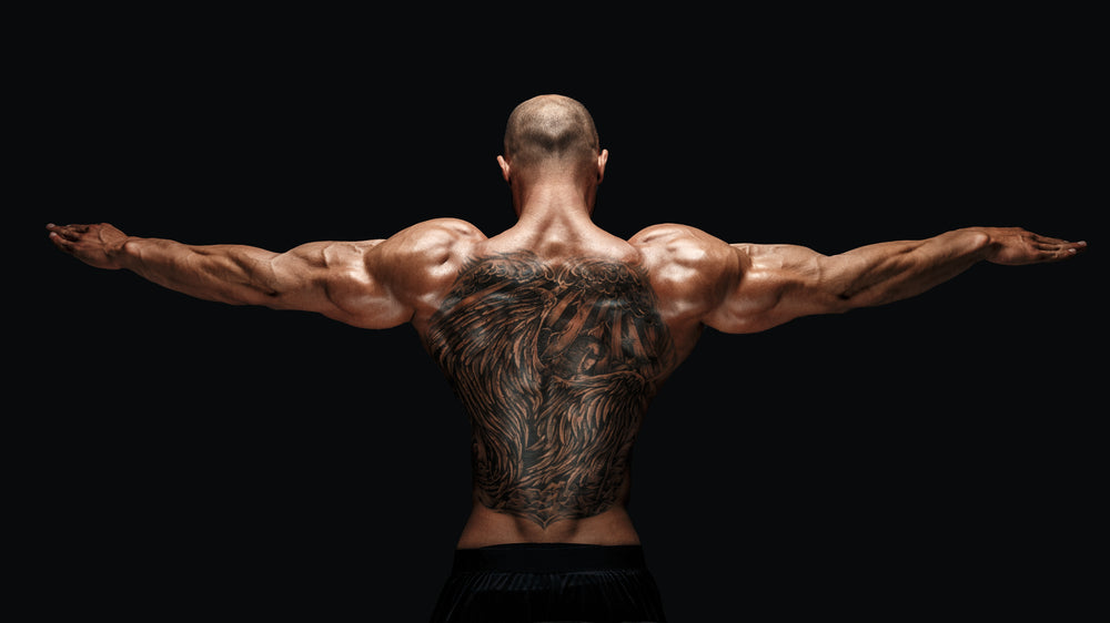 tattooed bodybuilder with outstretched arms on black background