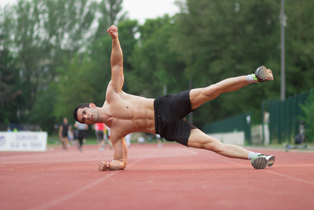Man doing side plank leg raise on a running track