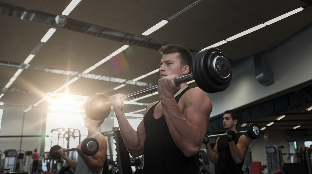 fit and muscular man doing wide grip barbell curls in a gym