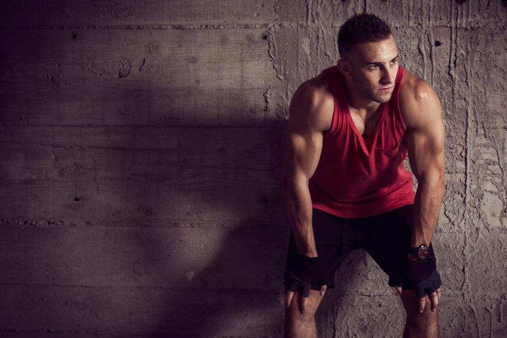 handsome athletic man sitting on cube with gym equipment around and clapping hands with talc before workout