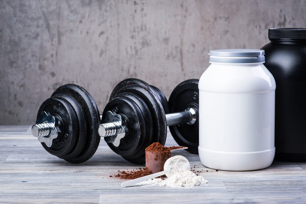black dumbbells next to two tubs of protein powder