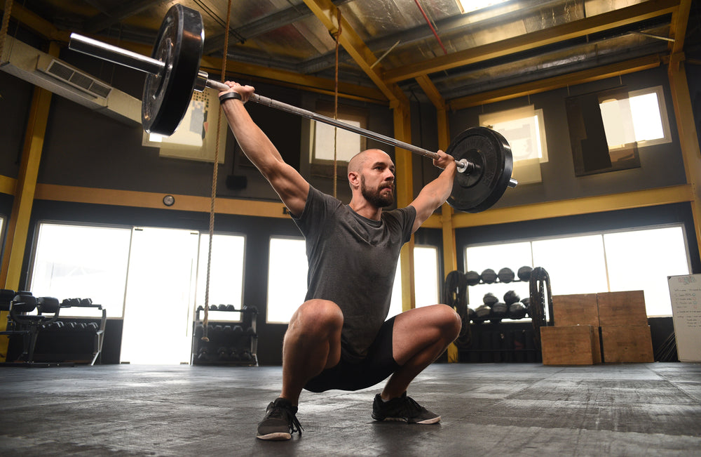 strong crossfit athlete in a heavy overhead squat lift in a cross-fit box gym