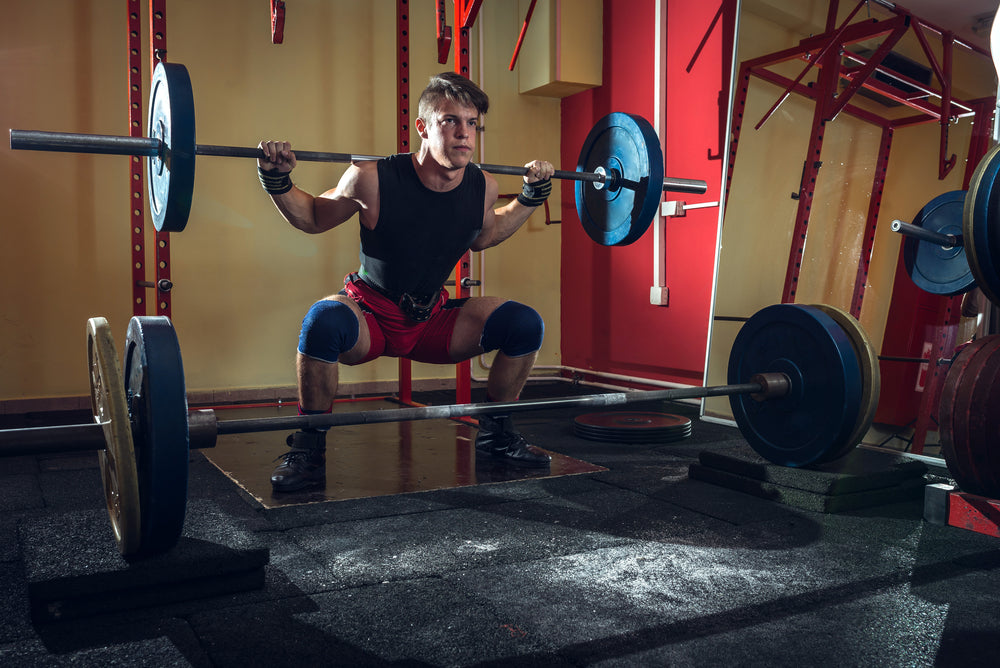 Young teenage man doing squats in indoor gym club.