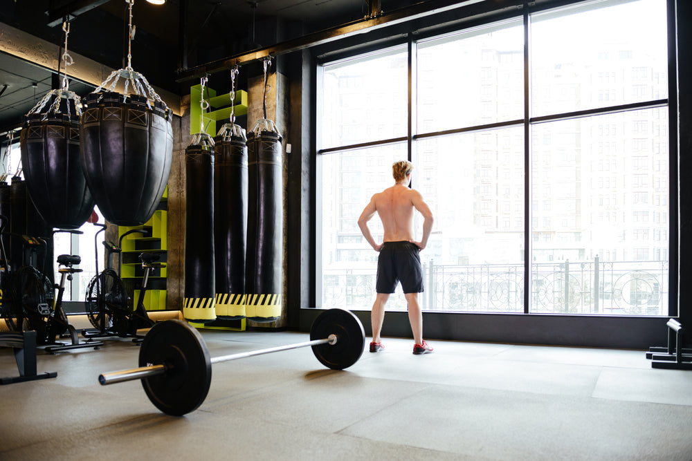 Portrait of Athletic man which standing near the window in gym with barbell