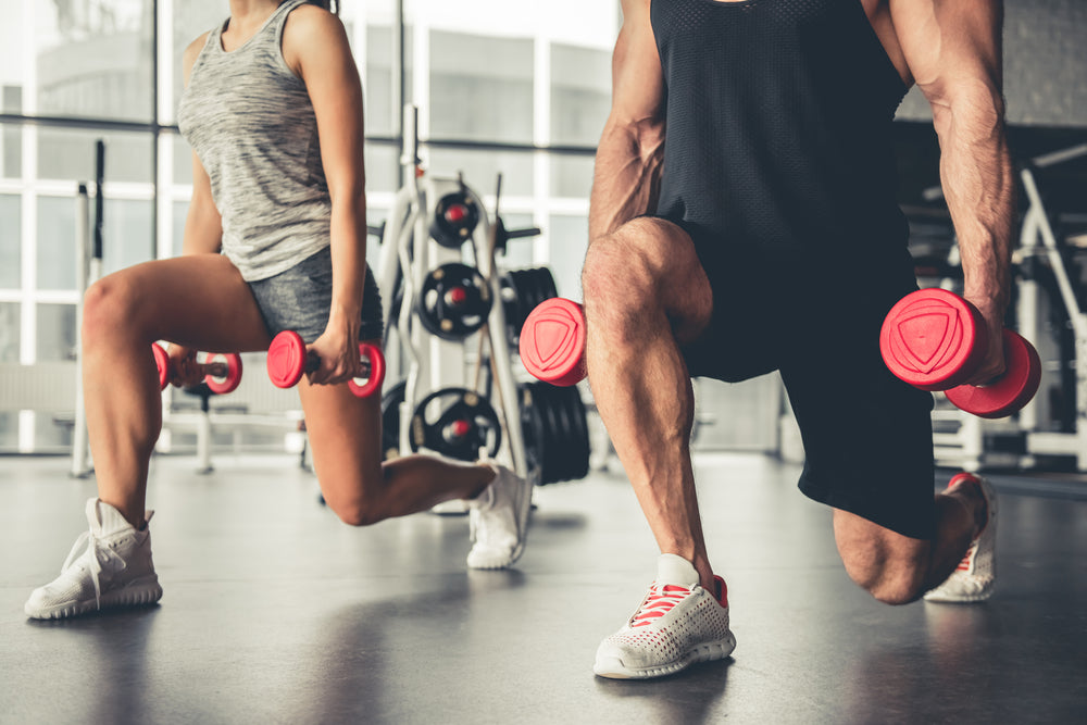 Attractive sports people doing dumbbell lunges in a gym