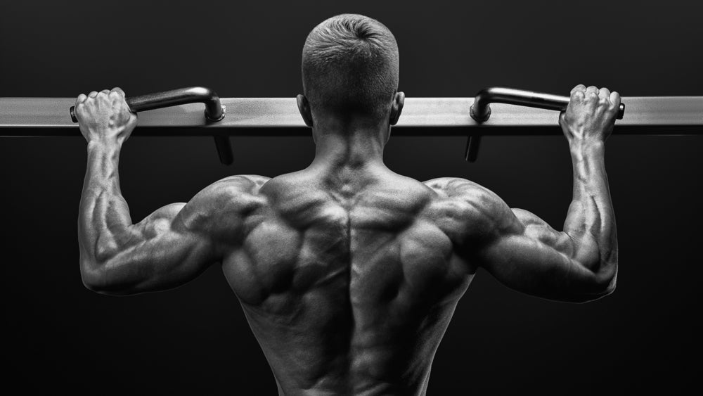 Black and white image of power muscular bodybuilder guy doing pullups in gym