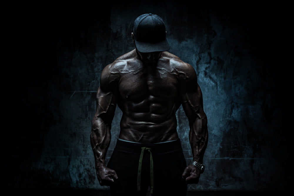 Young strong man bodybuilder in cap on stone wall background