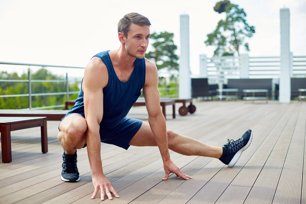 Handsome young sportsman doing side lunges outdoors